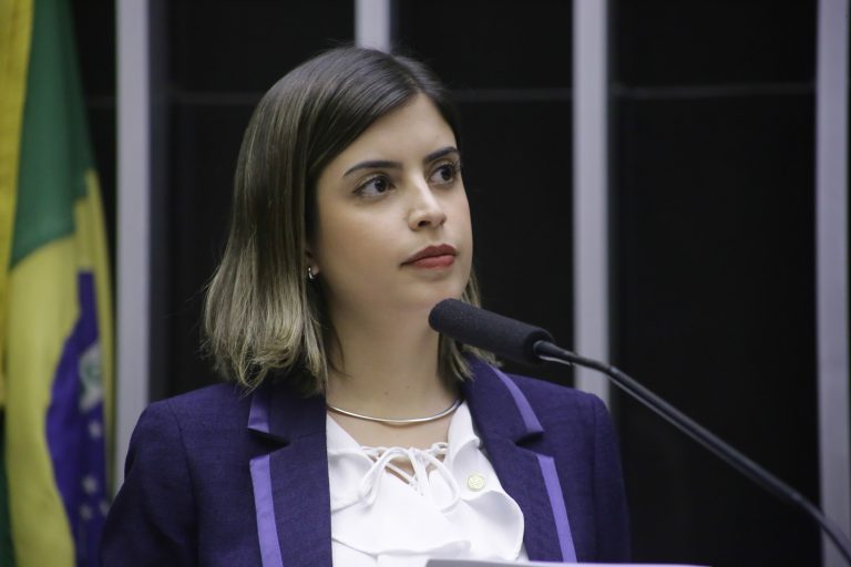 Deputada Tabata Amaral fala ao microfone. Ela é branca, tem o cabelo escuro, usa uma blusa banca e um blazer azul-marinho