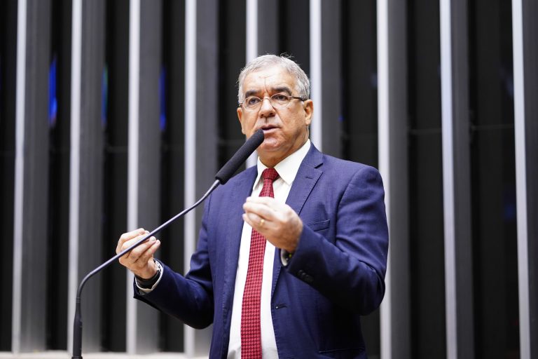 Deputado Zé Neto fala ao microfone. Ele tem cabelo grisalho e usa óculos e um terno azul-marinho