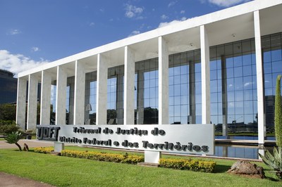 Fachada de um prédio espelhado com uma placa no gramado onde se lê: Tribunal de Justiça do Distrito Federal e dos Territórios