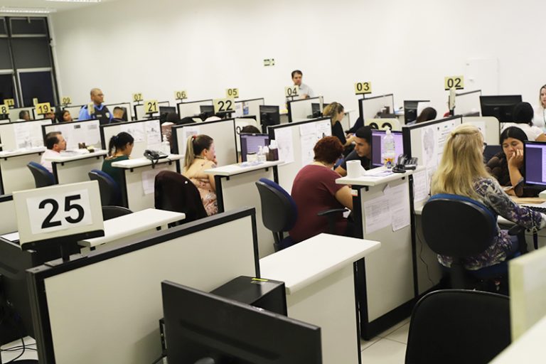 Várias pessoas estão trabalhando sentadas em mesas brancas e numeradas atendendo ao público