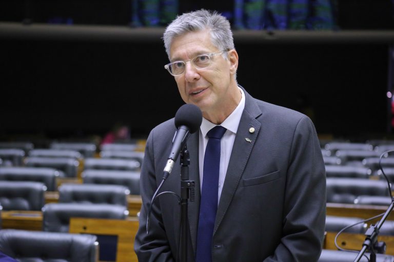 Deputado Guiga Peixoto discursa no Plenário da Câmara. Ele é branco, grisalho, usa terno cinza e óculos