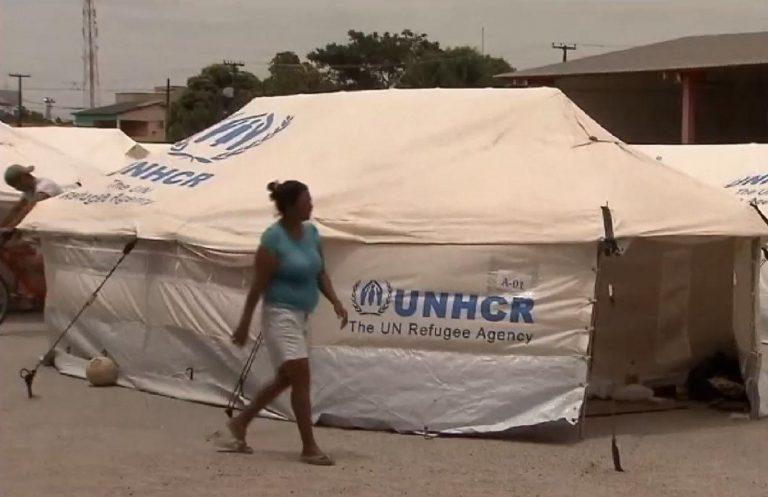 Barracas brancas da ONU e uma mulher caminhando na frente. O rosto dela está desfocado