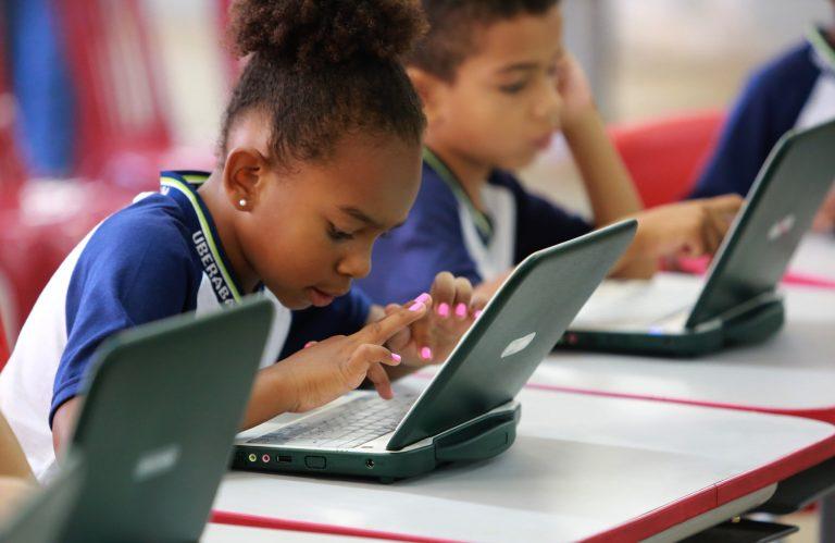 Alunos estudam num laptop. Eles usam uniforme azul e branco
