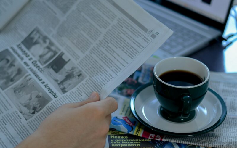 a person reading a newspaper with a cup of coffee