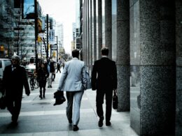 people walking on sidewalk pathway beside road with vehicles and high-rise buildings during daytime