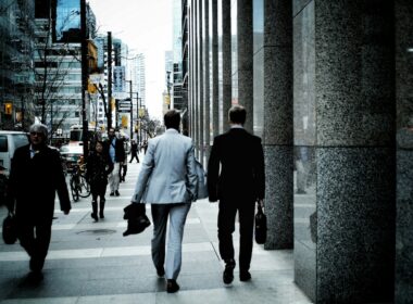 people walking on sidewalk pathway beside road with vehicles and high-rise buildings during daytime