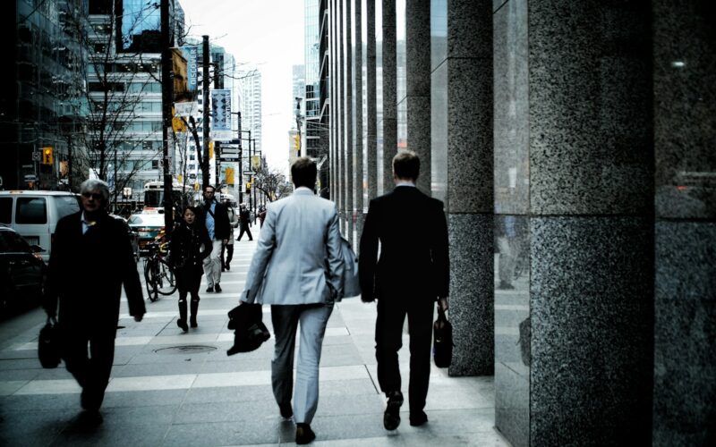 people walking on sidewalk pathway beside road with vehicles and high-rise buildings during daytime