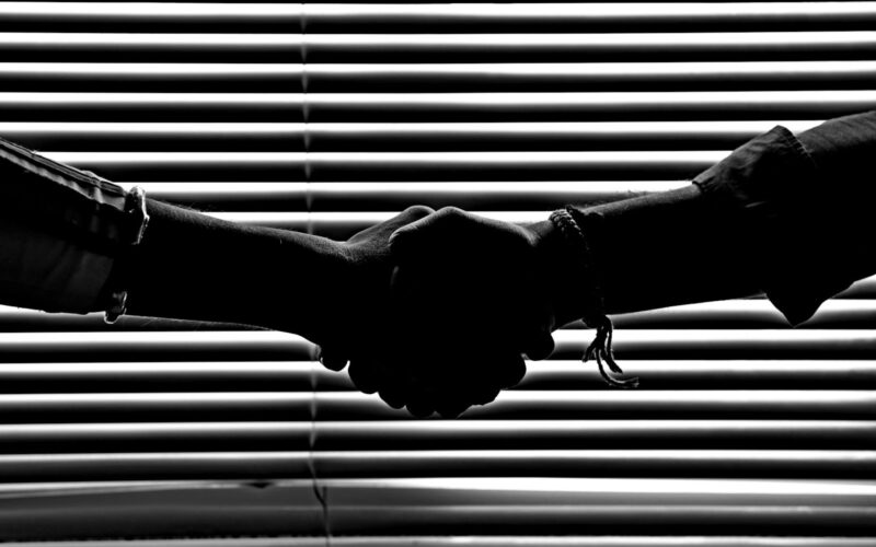 Silhouette of two people shaking hands symbolizing partnership and trust.