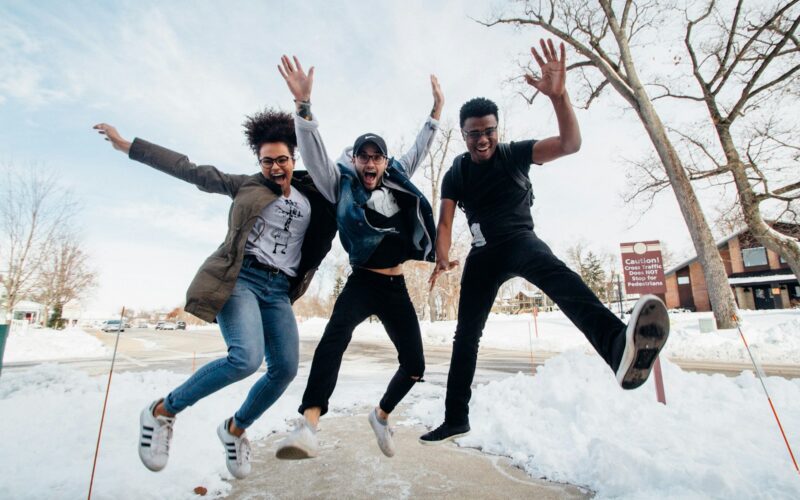 photo of three men jumping on ground near bare trees during daytime