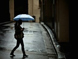 woman with tote bag holding umbrella while crossing street
