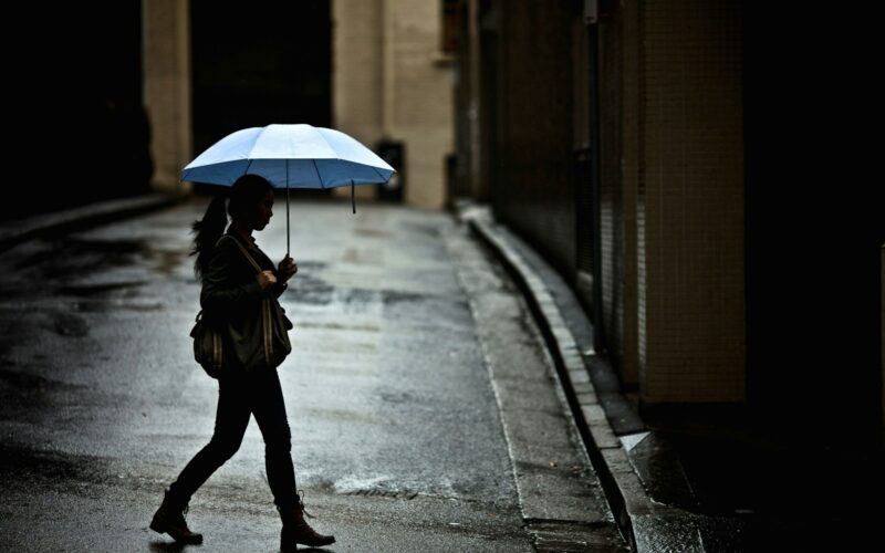 woman with tote bag holding umbrella while crossing street