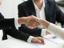 two people shaking hands in front of a laptop
