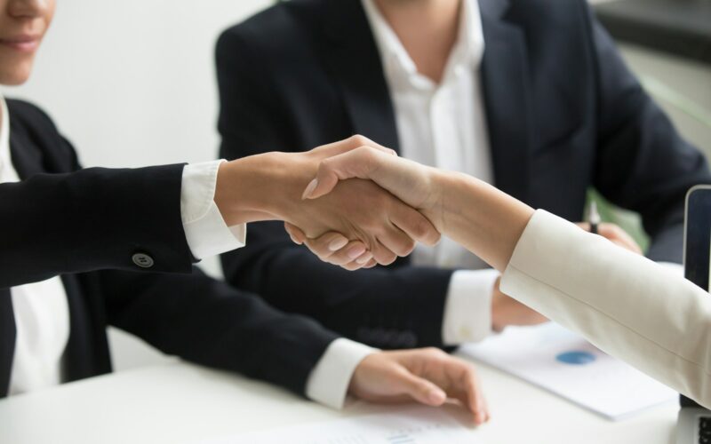 two people shaking hands in front of a laptop