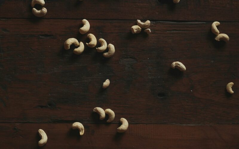 Cashews are scattered on a dark wooden surface.