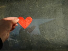 a hand holding a piece of paper with a heart cut out of it