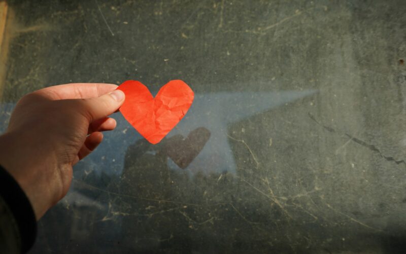 a hand holding a piece of paper with a heart cut out of it