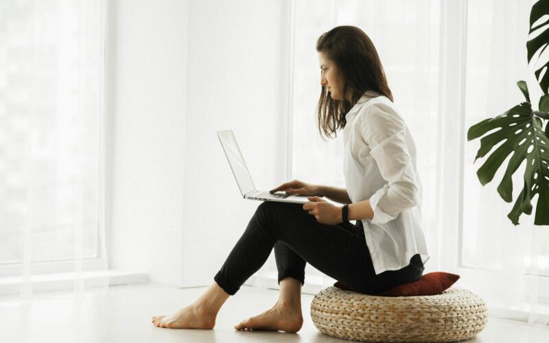 woman in white long sleeve shirt and black pants sitting on brown woven chair