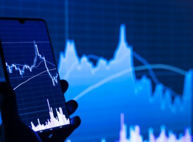 a person holding a cell phone in front of a stock chart