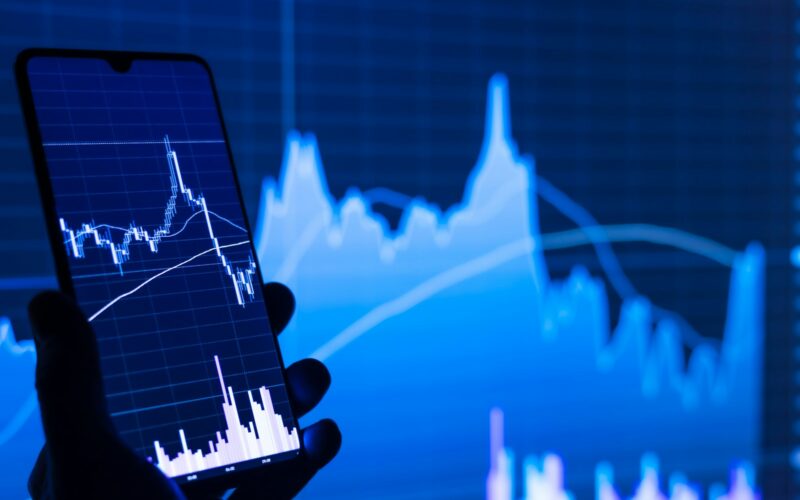 a person holding a cell phone in front of a stock chart