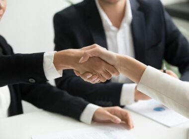 two people shaking hands in front of a laptop